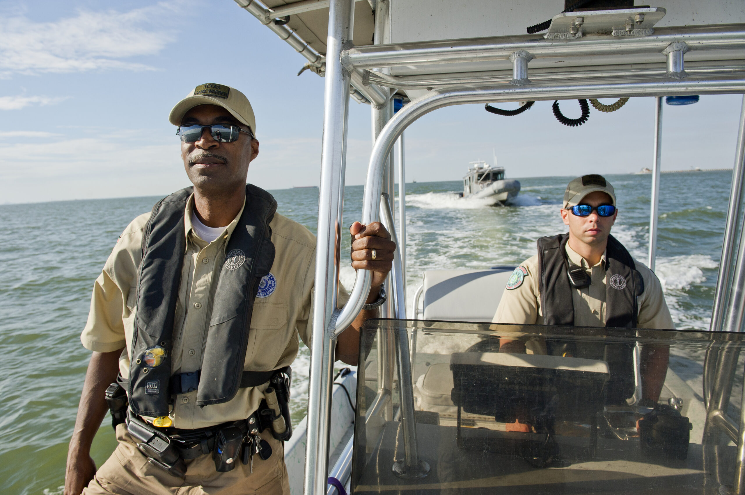 Texa game wardens stand in a boat on the ocean. The 287(g) program allows local officers to detain and transfer people to ICE and wildlife agencies are participating directly.