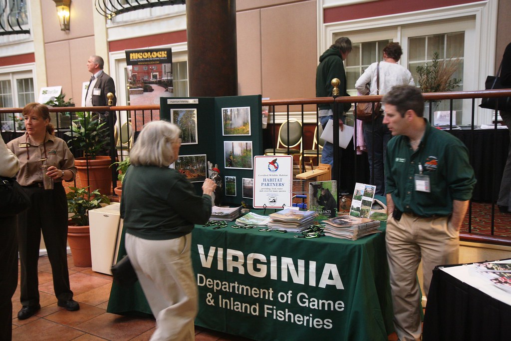 A member of the Virginia Department of Game stands in front of a table at a tradeshow. The 287(g) program allows local officers to detain and transfer people to ICE and wildlife agencies are participating directly.